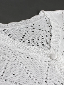 Detail of white hollow knit cardigan with ribbed collar and matching fabric button