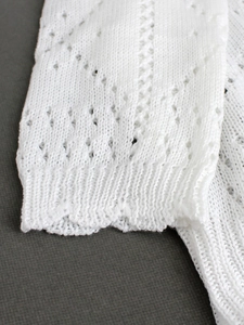 Detail of white V-neck cardigan featuring pointelle hollow knit and ribbed cuffs texture