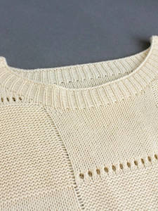 Close-up detail of cream knit sweater showing round ribbed neckline and hollow-out patterns