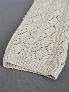 Close-up of cream knit fabric with diamond hollow pointelle pattern and soft texture