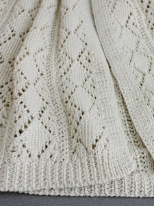 Detail of hollow diamond knit pattern and ribbed edges on a creamy white knit shawl