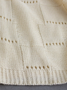 Detail of beige knit fabric featuring square textures, eyelet holes, and ribbed hemline