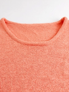 Detailed close-up of coral orange knit sweater vest showing round neckline and thick texture