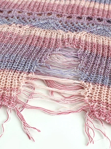 Détail du tissu en maille ajourée rose et violette avec bords effilochés sur le gilet
