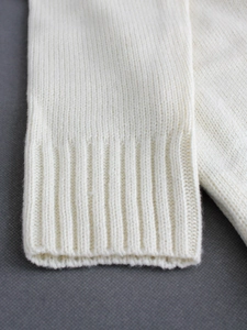 Macro shot of ribbed cuffs on a white V-neck sweater showing premium knit texture
