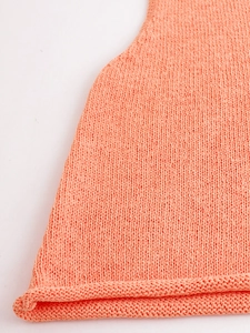 Detailed macro view of vibrant coral orange knit fabric with rolled hem edge finishing