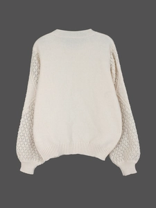 Detail of white knit sweater showing intricate hollow-out lace sleeves and ribbed cuffs