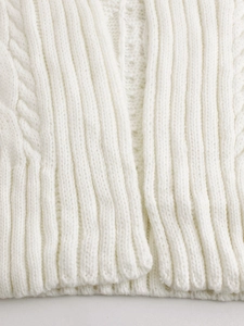 Detailed close-up of chunky cable knit pattern and ribbed hem on a white cardigan