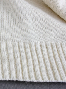 Detailed close-up of white knitted sweater texture and elastic ribbed hem finish