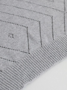 Detail of light gray knit sweater showing geometric pointelle patterns and ribbed edges