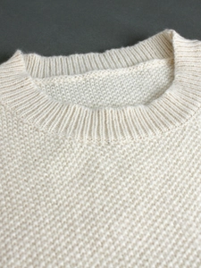 Detailed macro view of cream knit sweater featuring ribbed crew neck and waffle texture