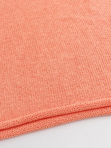 Close-up of bright coral knitted fabric with detailed texture and neat rolled hem edges