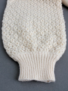 Detailed macro shot of a cream knit sweater featuring honeycomb texture and ribbed cuffs