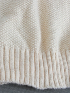 Close-up of cream knit sweater showing textured honeycomb stitch and ribbed hem detail