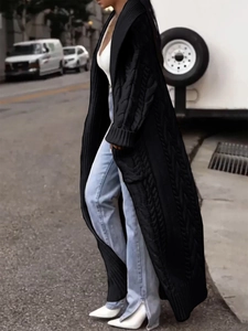 Detail of a long black cable-knit cardigan featuring a wide lapel and deep functional pockets