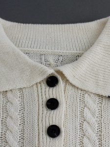 Macro shot of cable-knit polo collar and black buttons on beige knitted top