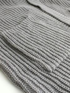 Macro detail of thick grey ribbed knit fabric texture and pocket seam of the cardigan