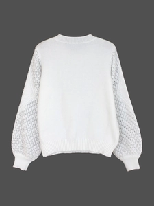 Detail of white knit sweater showing intricate hollow-out lace crochet on long sleeves