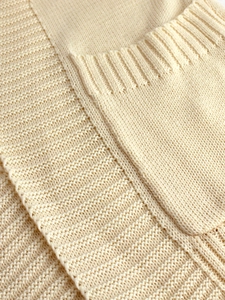 Detailed close-up of beige knitted cardigan showing ribbed edges and a high-quality pocket