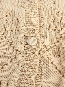 Detailed macro view of beige pointelle knit cardigan with fabric-covered button