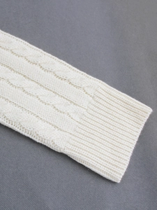 Detailed macro view of the thick white cable knit texture and ribbed cuff design