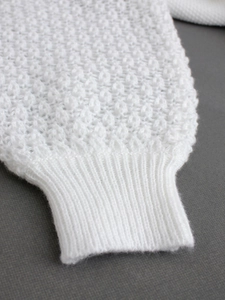 Macro detail of white knit sweater cuff featuring pointelle patterns and ribbed trim