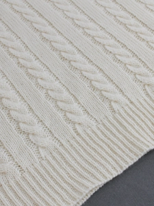 Detailed view of white cable knit texture and ribbed hem on a cozy winter sweater