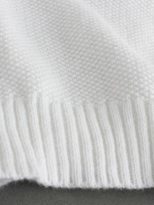 Close-up of white knit sweater showing high-quality ribbed cuff and texture details