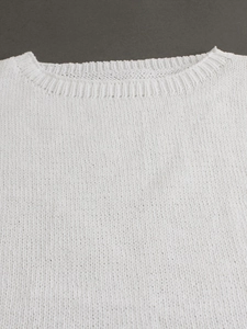 Detailed close-up of white knitted vest showing soft cotton texture and ribbed crew neck
