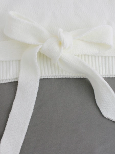 Detailed view of white knit sweater featuring a bow tie and ribbed cuff texture