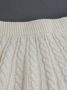 Close-up of cream white cable knit texture and elastic ribbed waistband on soft fabric