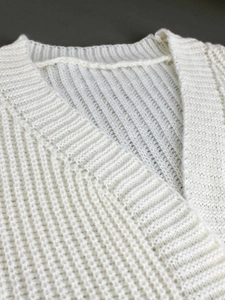 Detail of white knit cardigan showing textured V-neckline and soft ribbed fabric weave
