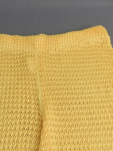 Detailed macro view of yellow knit beach trousers showing hollowed-out crochet texture
