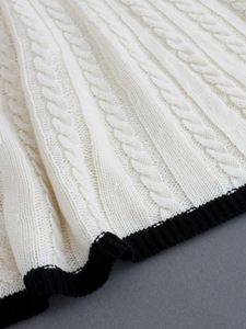 Close-up of white cable-knit sweater detail with a contrasting black ribbed hem design