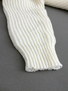 Close-up of white chunky knit sweater cuff with ribbed texture on grey background
