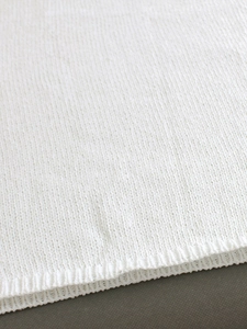 Detailed close-up of white knitted vest showing fine jersey stitch and ribbed hem