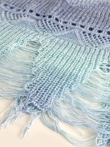 Détail de la texture tricotée et des franges d'un gilet de plage bleu dégradé pour femmes