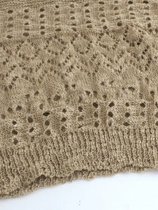 Makro-Detail des khakifarbenen Strickstoffs mit floralem Lochmuster und Rippbündchen