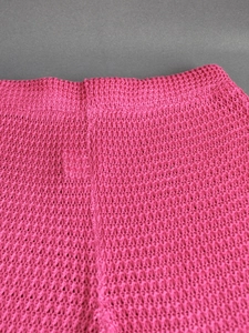 Close-up of bright pink crochet knit beach pants showing hollow-out geometric texture