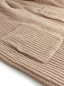Detailed macro view of the thick knit texture and square pocket on a beige cardigan