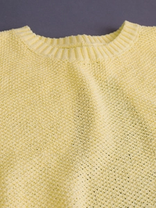 Light yellow knit sweater vest with crew neck and honeycomb texture on grey background