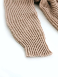 Detailed macro view of the ribbed cuffs on a chunky knit camel cardigan sweater
