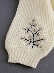 Gros plan d'un pull à col roulé blanc cassé avec broderie botanique marron élégante