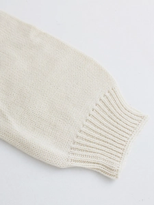 Detail of soft cream knit sweater sleeve showing ribbed cuff and thick textured fabric