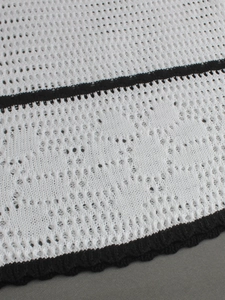 Detail of white hollow crochet knit fabric with black contrast trim and intricate pattern