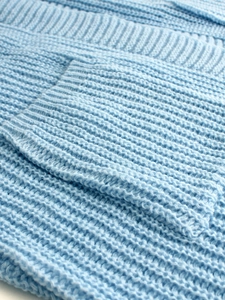 Detailed close-up of thick ribbed knit fabric and front pocket on light blue cardigan