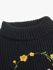 Gros plan d'un pull noir à col montant avec broderie florale jaune et maille épaisse
