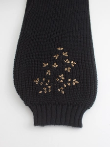 Détail de la manche en maille noire avec broderie florale dorée et bordure côtelée