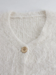 Detailed close-up of cream knit cardigan with V-neck, plush texture and wooden button