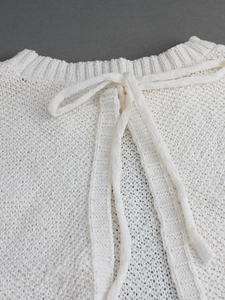 Close-up of white knitted halter top featuring lace-up neck ties and hollow out texture